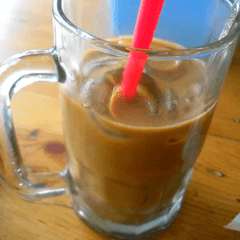Foto es kopi susu dalam gelas mug kaca dengan sedotan merah di meja kayu