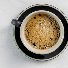 Foto espresso dengan crema di cangkir putih dan tatakan hitam, dilihat dari atas